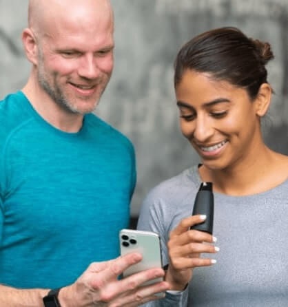 2 smiling people one holding a phone and the other holding a Lumen device